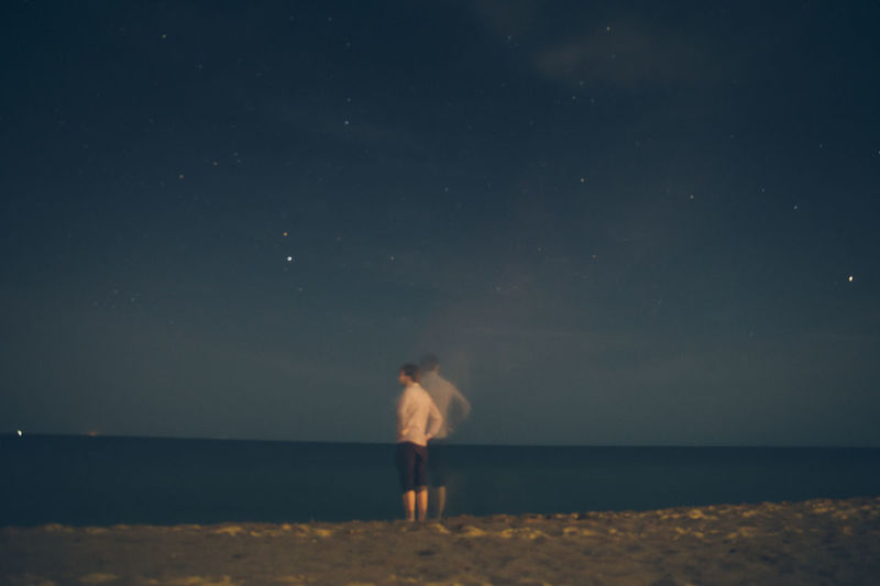 Rear view of boy standing on beach against sky at night