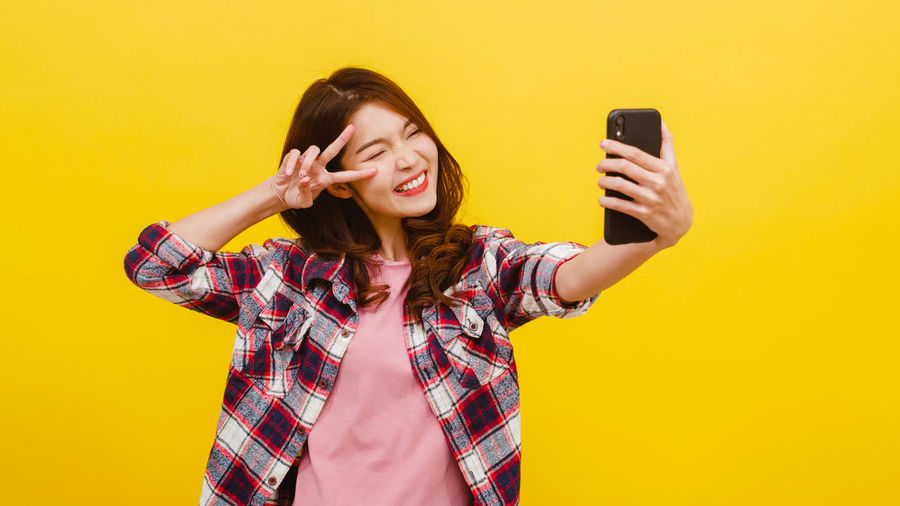 Young woman using mobile phone against yellow background
