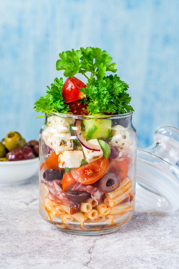 Salad with pasta, fresh vegetables, salami, olives and feta cheese in a jar - healthy lunch idea
