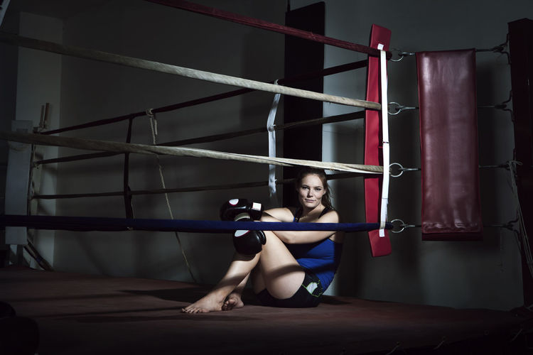 Tired sportswoman sitting in boxing ring at gym