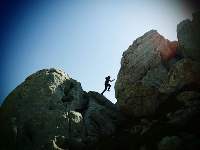 Low angle view of man jumping on rock against sky