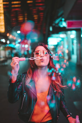 Portrait of young woman wearing sunglasses standing at night