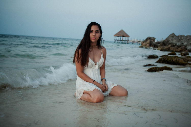 Full length of teenage girl kneeling on shore at beach