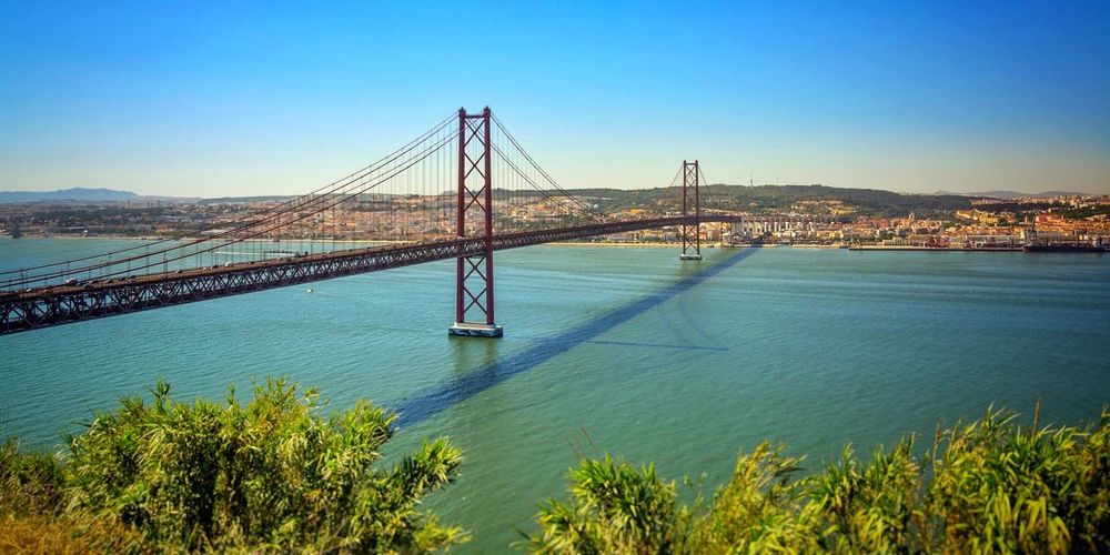 April 25th bridge over tagus river by city against clear sky