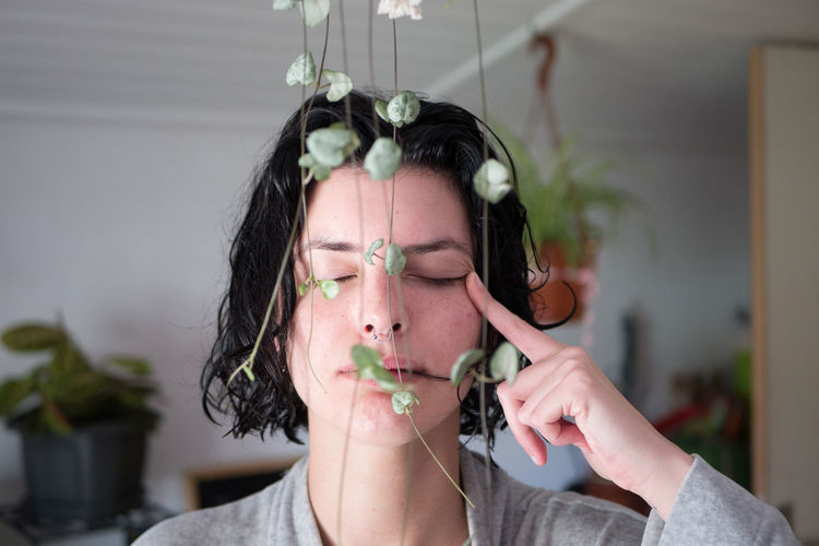 Woman with closed eyes by plants at home