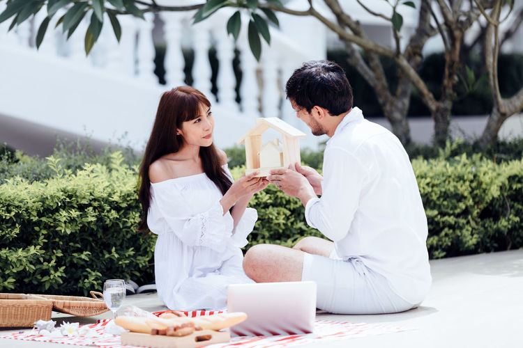 Couple holding model home while sitting by plants
