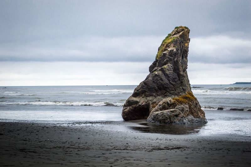 Rock on wet shore against cloudy sky