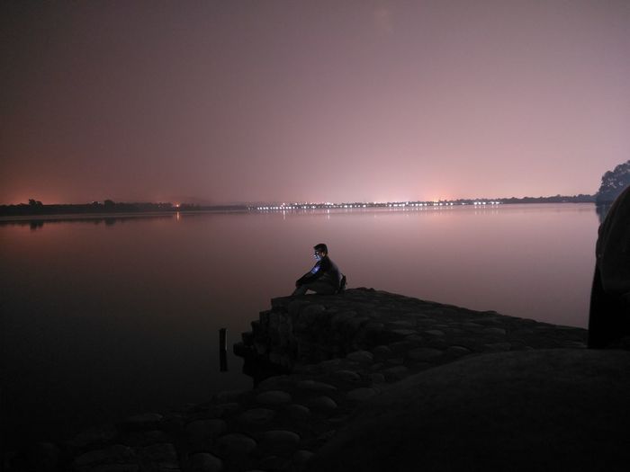 Man sitting by lake on rock at night