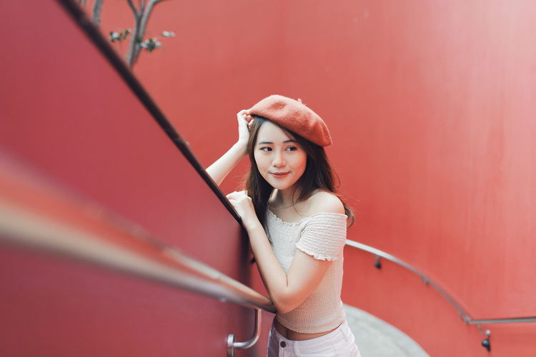 High angle view of thoughtful young woman standing at railing against red wall