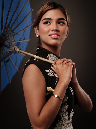 Portrait of young woman holding umbrella against black background