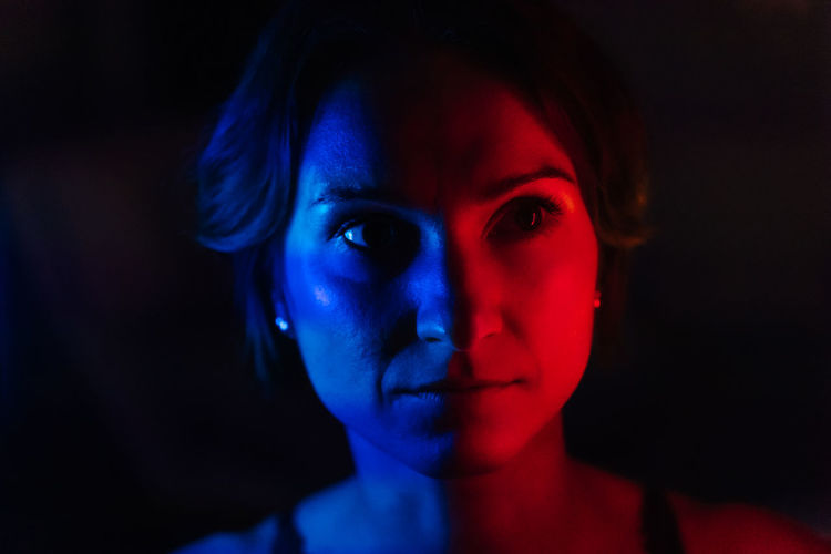 The face of a young woman in blue and red neon light on a dark background
