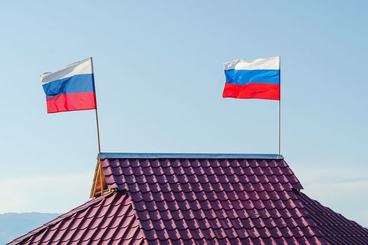 Two russian flags are developing on the roof of the house against the sky.