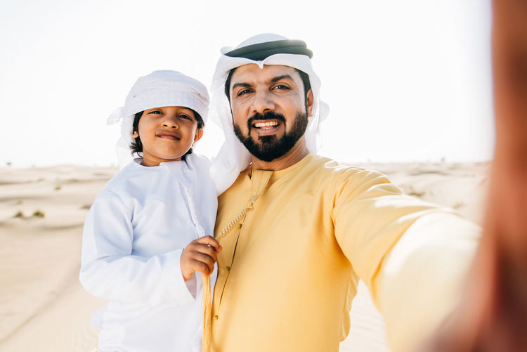 Portrait of father and son doing selfie while standing at desert