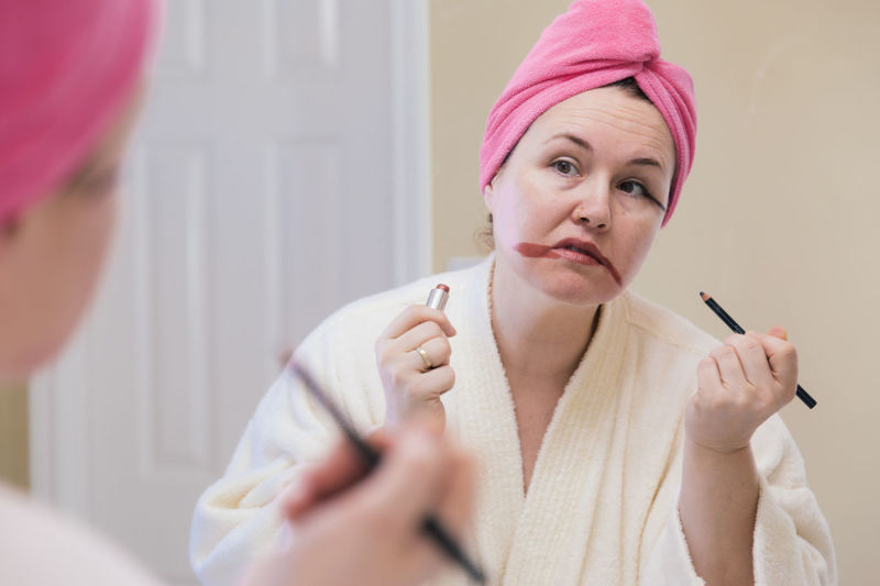 Mature woman applying make-up reflecting on mirror at home