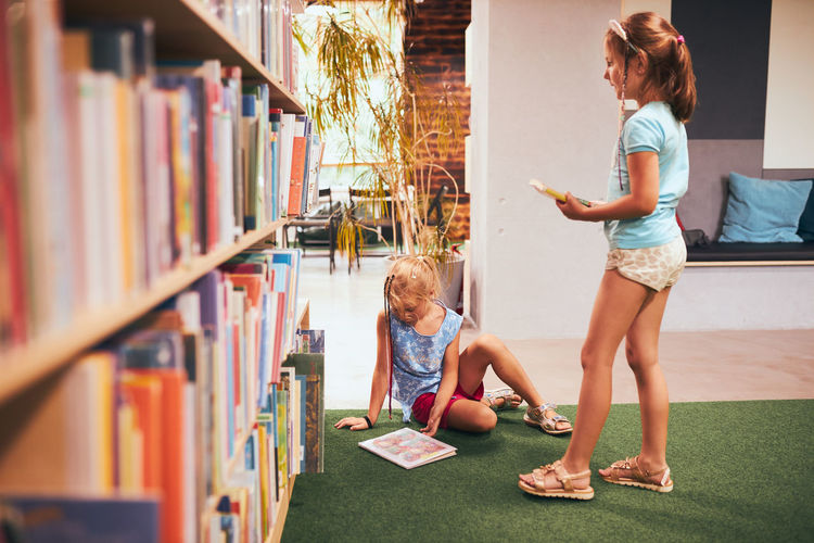 Schoolgirls looking for book for reading in school library. students choosing books to read