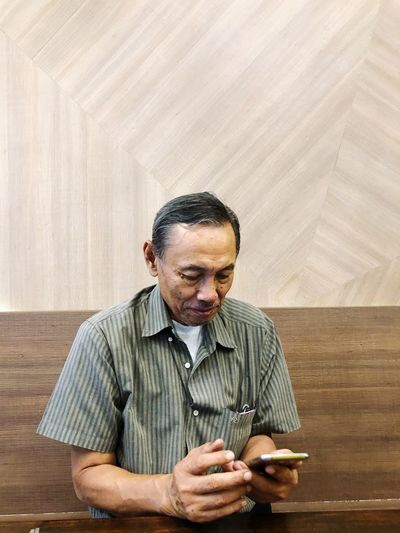 Senior man using mobile phone against wall at home
