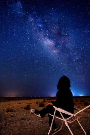 Rear view of woman sitting against sky at night
