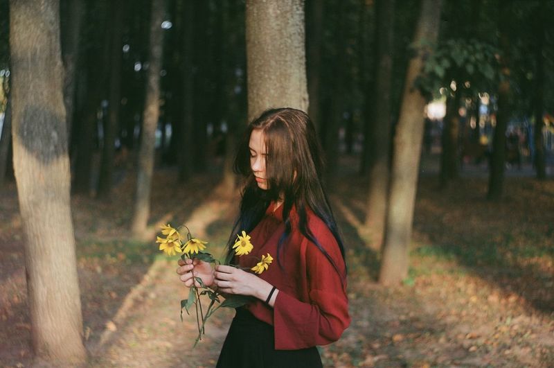 Young woman holding flowers while standing in forest