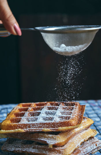 Cropped hand of woman putting powdered sugar on waffles at table