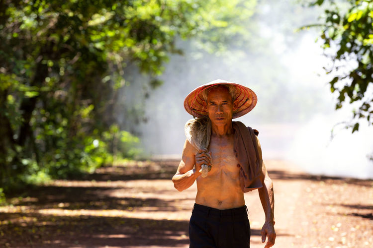 Portrait of senior man wearing conical hat standing on dirt road