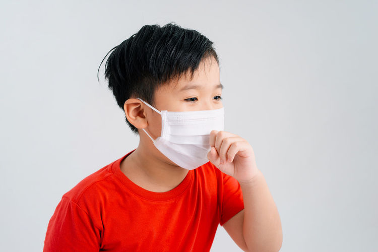 Boy wearing pollution mask coughing against white background