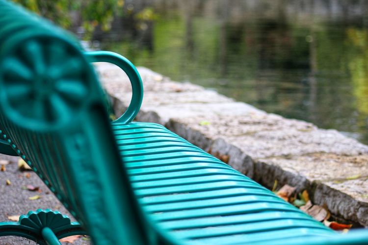 A close up view of an empty green park bench by a pond with blurred vision in the background.