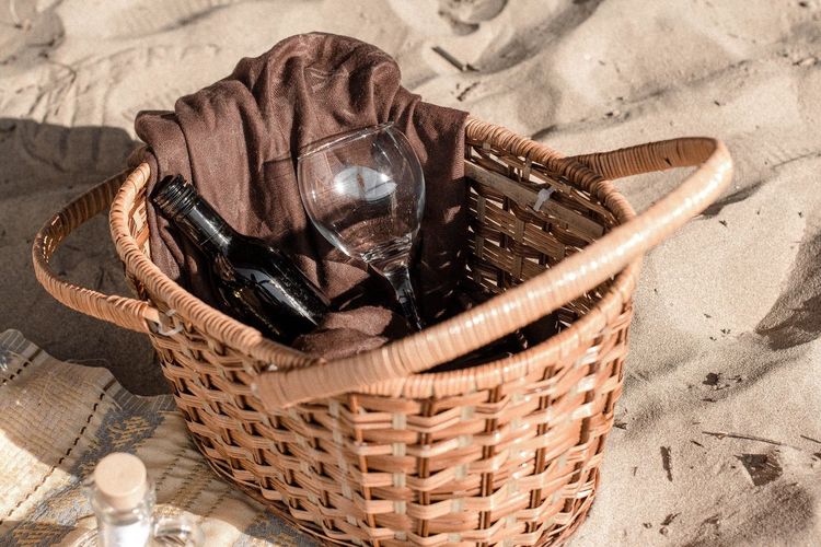 High angle view of wine bottle and glass in wicker basket on sand