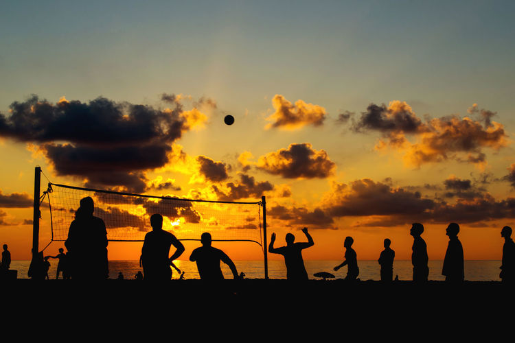 Silhouette people playing volleyball at beach against sky during sunset