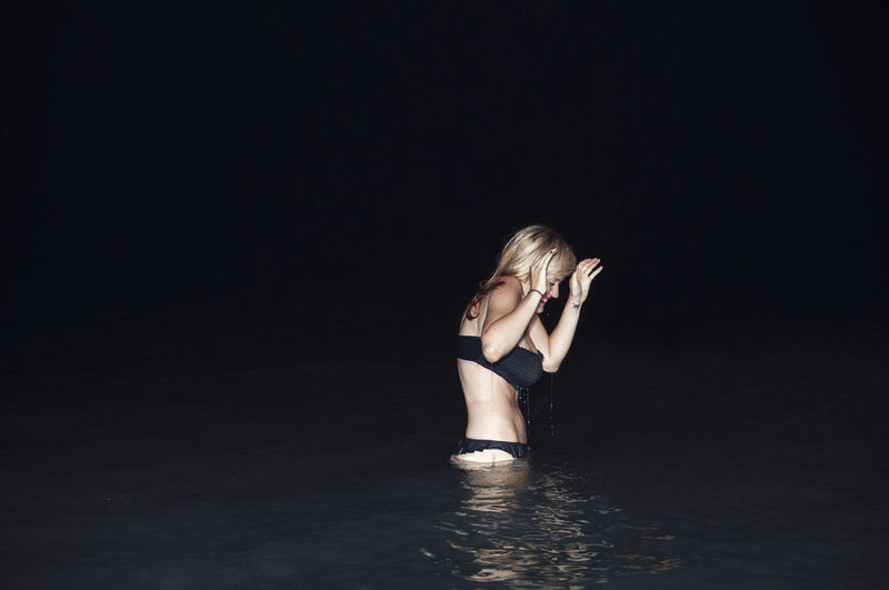 Woman with eyes closed standing in lake at night