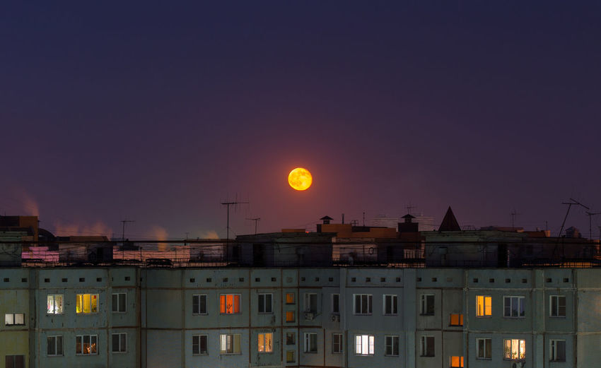 Windows, roofs and facade of an mass apartment buildings in russia at full moon night. 