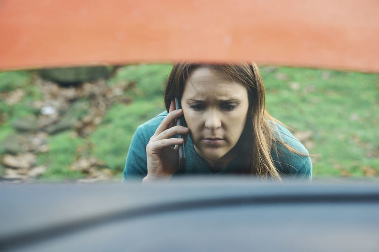 Sad or angry beautiful woman calling insurance or tow truck for car 