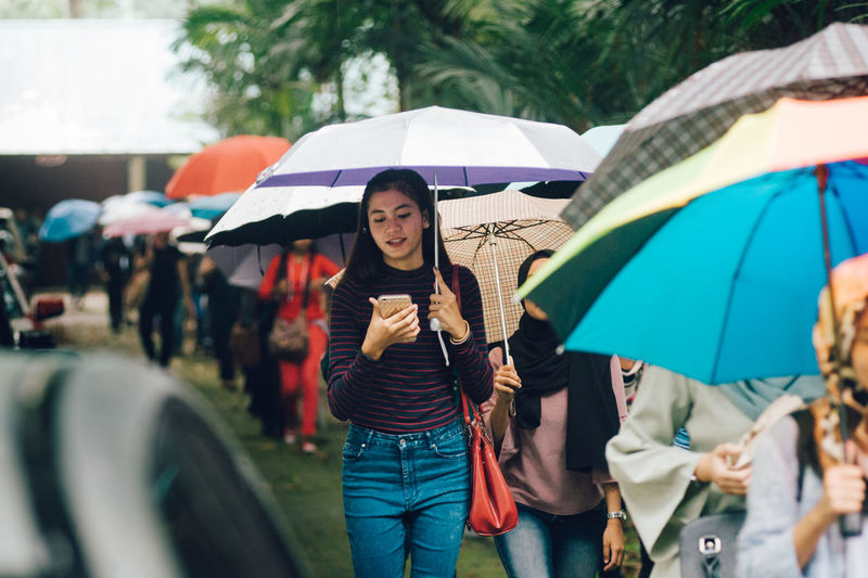 Woman using mobile phone while holding umbrella