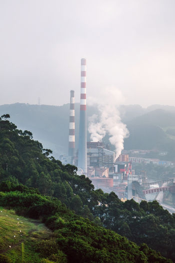 Green grassy slope against hazy industrial factory with smoke from pipes