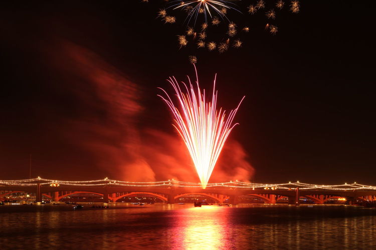 Low angle view of firework display over river against sky