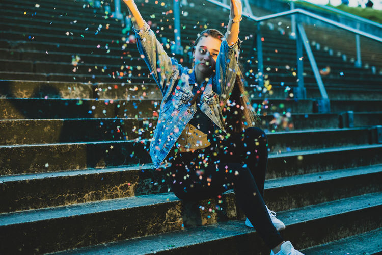 Woman throwing confetti while sitting on staircase