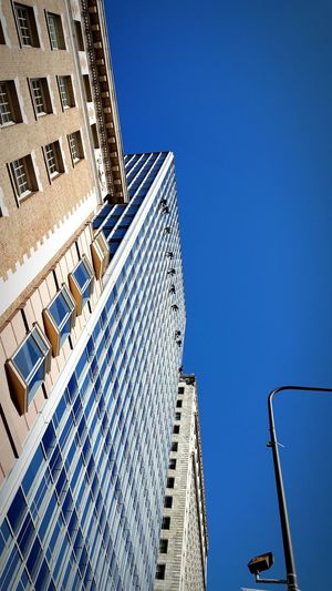 Low angle view of window washers on modern building against clear sky