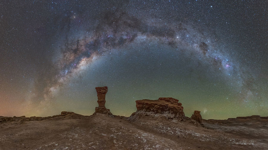 Panorama of strange salty rock formations in atacama desert against night sky with milky way arc