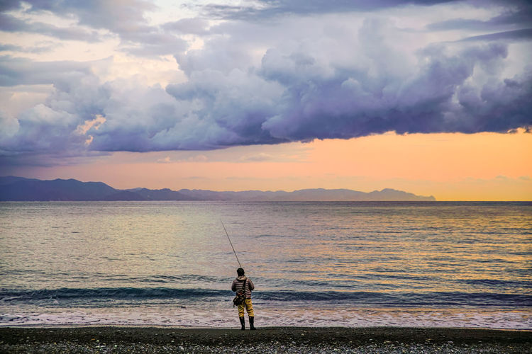 Men fishing in sea against sky during sunset