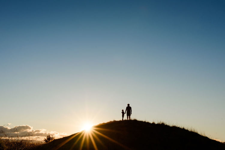 Silhouette of father and son at the top of a hill at sunset
