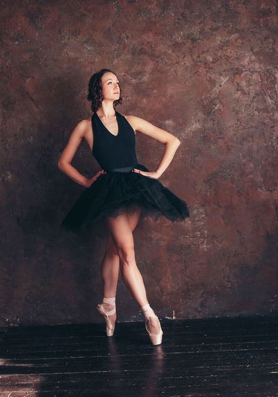 Full length of young woman with hands on hip dancing against wall in dance studio
