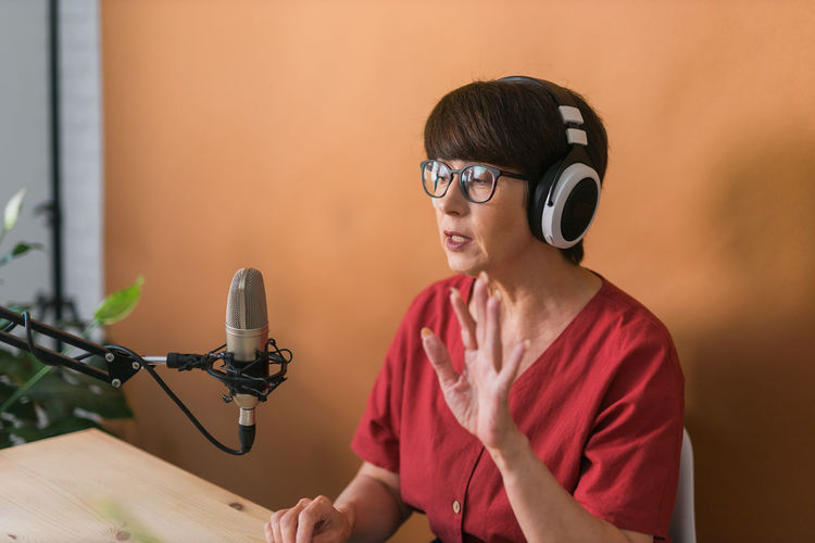 Senior woman podcasting against wall