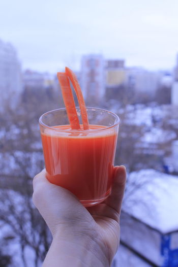 Cropped hand holding drink carrot juice on the background of winter city