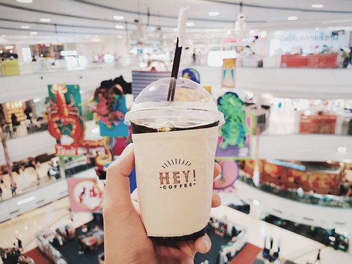 Cropped hand holding disposable cup in shopping mall