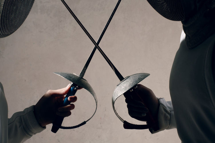Close-up of people holding swords while fencing against wall
