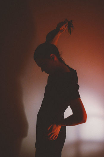 Side view of young woman holding ponytail by wall at home