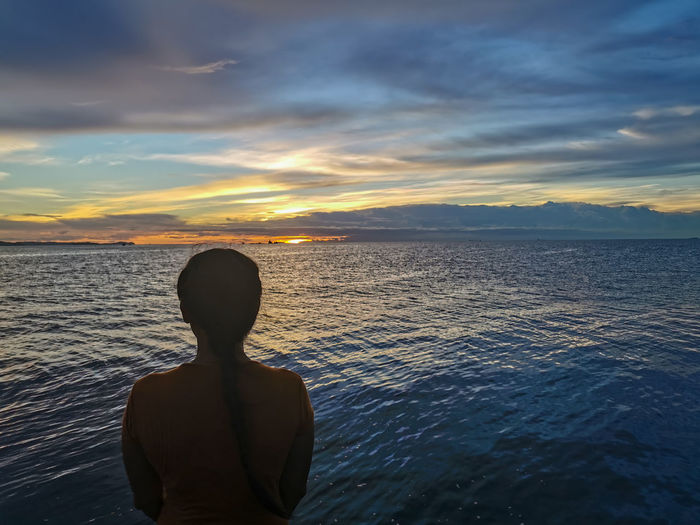 Rear view of beautiful girl looking at sea against sunset sky