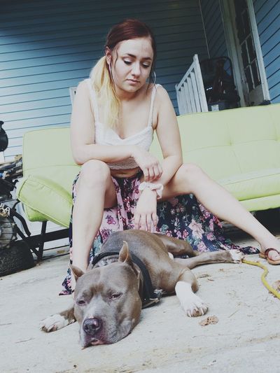 Low angle view of teenage girl looking at dog lying on floor while sitting outdoors