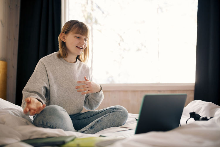 Teenage girl gesturing while attending video call during homeschooling in bedroom