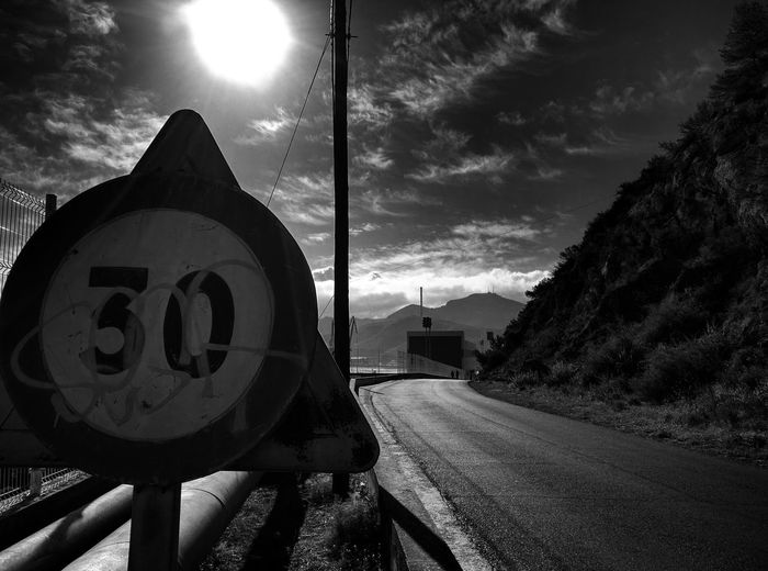 Speed limit sign by road against sky