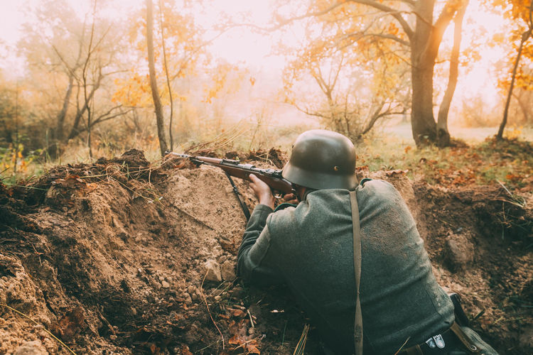 Rear view of army soldier with rifle in forest